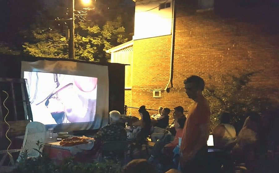 A group of people watching a movie projected onto a sheet outside.