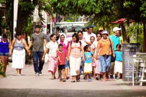 Photograph of a group of people, adults and children, walk together along a sunny street